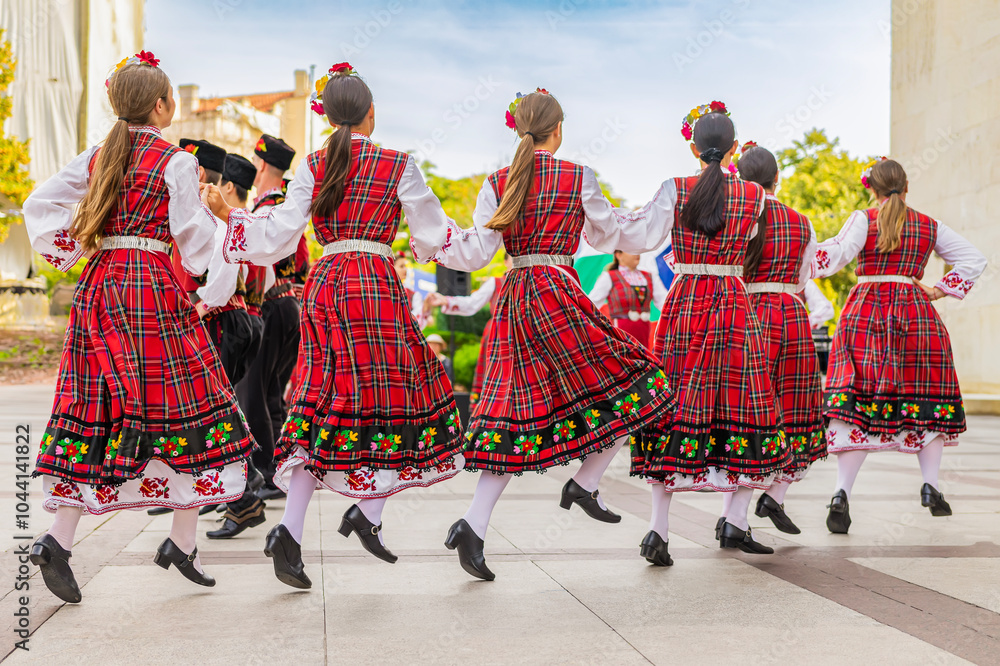 Naklejka premium Rear view of group of dancers wearing traditional folk dresses dancing on cultural festival