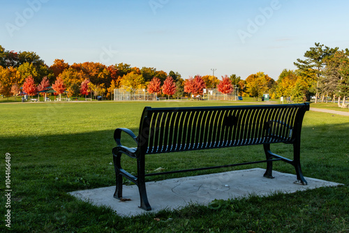 Foodball and basketball fields surrounded by colorful fall foliage,  a black metal bench in the foreground  photo