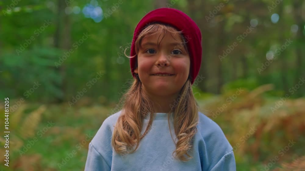 Portrait of a beautiful little girl of 5 years old in a red hat smiling at the camera standing against the background of a sunny forest in autumn Portrait of a beautiful little girl of 5 years old in a red hat smiling at the camera standing against the background of a sunny forest in autumn