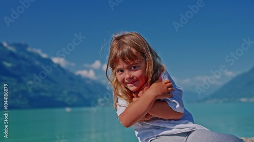 Little girl holding a small soft teddy bear with the image of the Swiss flag as a symbol of Switzerland against the background of the beautiful lake Interlaken in the city of Brienz photo