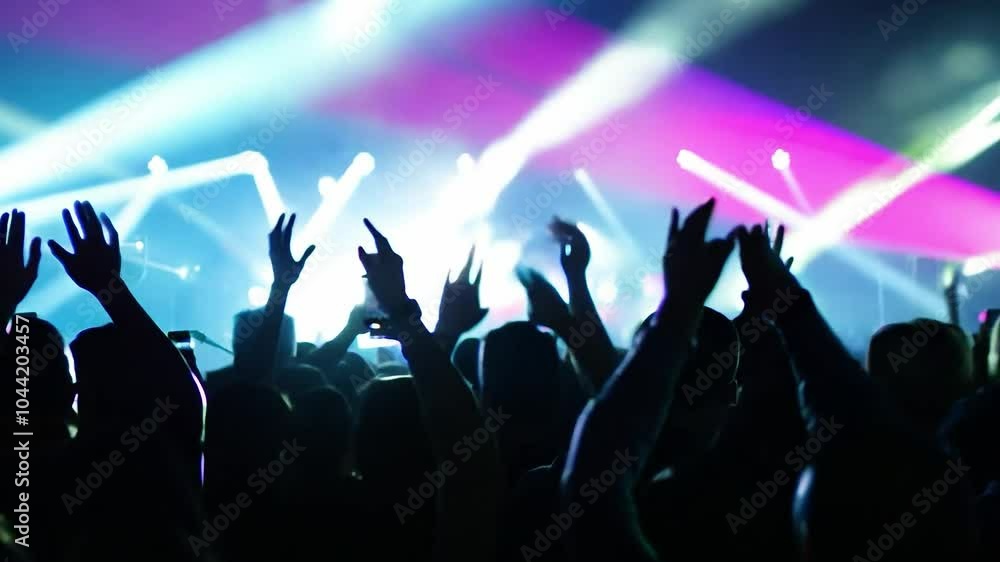 Crowd cheering and waving hands at a vibrant concert, illuminated by colorful stage lights, creates an electrifying atmosphere Crowd cheering and waving hands at a vibrant concert, illuminated by colorful stage lights, creates an electrifying atmosphere
