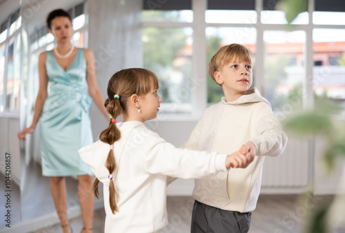 Boy with pair girl in sport wear train to dance vigorous hustle during classes. Children rehearse contemporary dancing movement. Female teacher conducts class for students photo