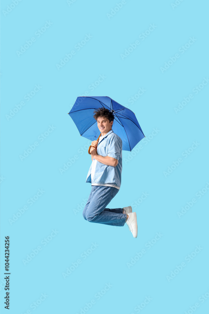 Young man with umbrella jumping on blue background Young man with umbrella jumping on blue background