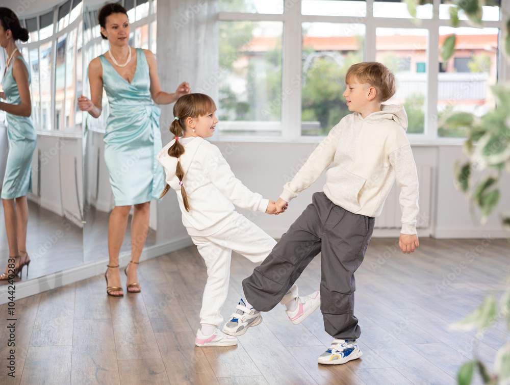 Fototapeta premium Happy couple of preteen dancers in sportswear practicing vigorous lindy hop at dance rehearsal with female coach controlling technique in choreography studio..