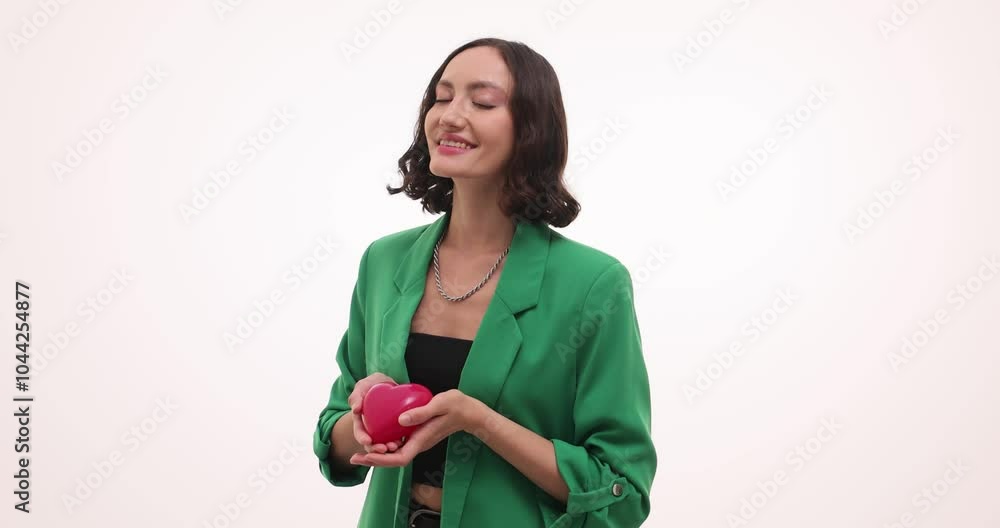Happy woman in green suit holds red heart toy on white background. Smiling young female expresses positive emotions holding cute present Happy woman in green suit holds red heart toy on white background. Smiling young female expresses positive emotions holding cute present