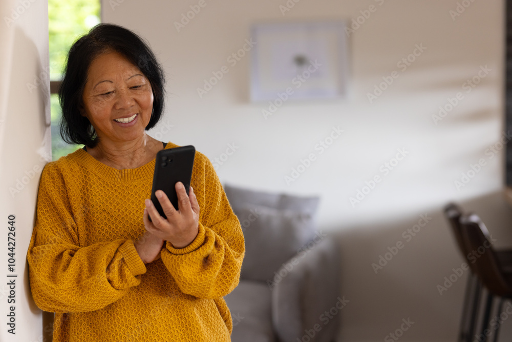 Smiling asian senior woman using smartphone at home, enjoying quiet moment Smiling asian senior woman using smartphone at home, enjoying quiet moment