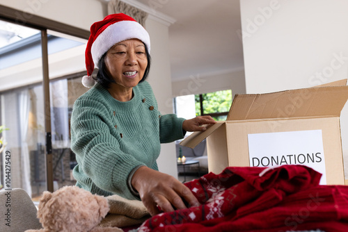 asian senior woman wearing Santa hat packing donations at home during Christmas photo