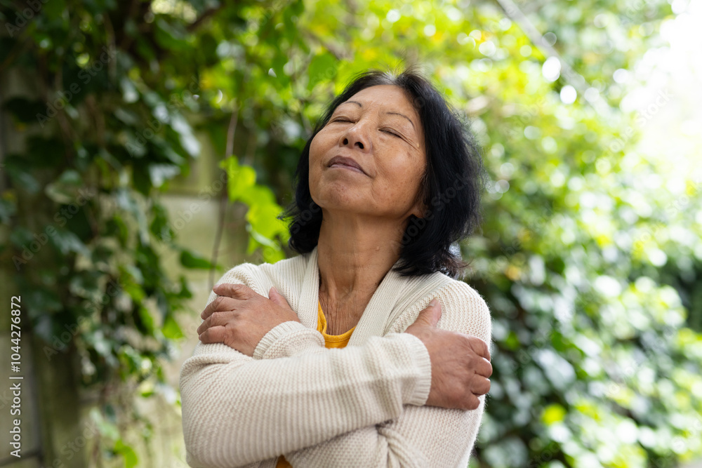 asian senior woman embracing herself outdoors, enjoying peaceful solitude in nature asian senior woman embracing herself outdoors, enjoying peaceful solitude in nature