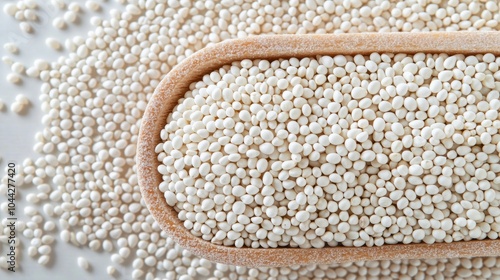 Close-up of white tapioca pearls in a wooden spoon, scattered on a white background.