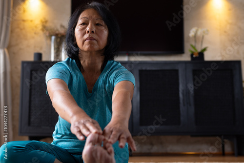 Asian senior woman practicing yoga at home, stretching and focusing on flexibility
