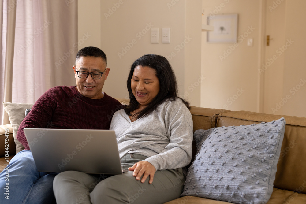 Smiling Senior multiracial couple using laptop on couch at home, enjoying time together Smiling Senior multiracial couple using laptop on couch at home, enjoying time together