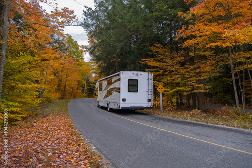 Camper van truck driving on a road surrounded by colorful maple trees with bright yellow leaves in fall season. Killbear Provincial Park, Ontario, Canada.