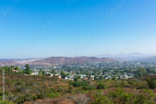 A scenic view from Big Rock Trail overlooking Santee, California, nestled among arid hills and natural vegetation, with distant mountains under a clear blue sky.