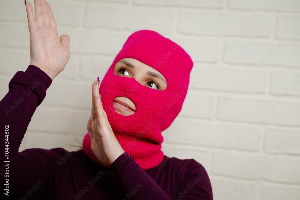 A woman wearing a bright pink balaclava dances energetically, striking unique poses with her hands against a clean, white brick wall background A woman wearing a bright pink balaclava dances energetically, striking unique poses with her hands against a clean, white brick wall background