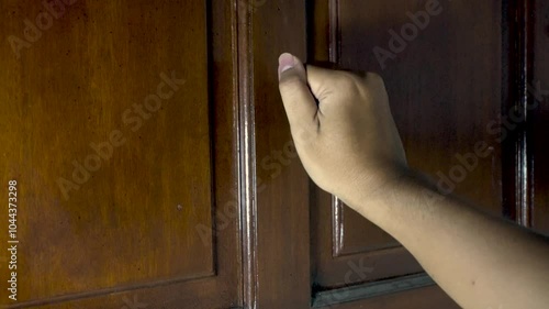 asian man's hand is knocking on the brown door