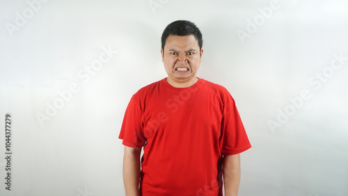 A young Indonesian man wearing a red t-shirt with an angry face facing forward