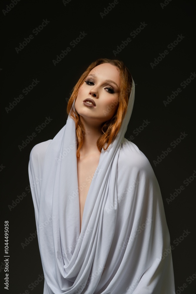 Woman draped in elegant white fabric poses against a dark background Woman draped in elegant white fabric poses against a dark background