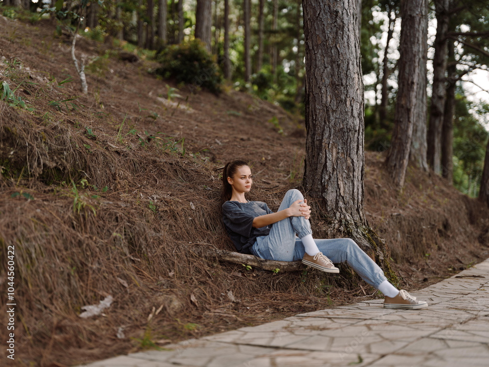 Thoughtful young woman sitting on a path in the forest, surrounded by trees, enjoying a moment of peace and reflection amidst nature Thoughtful young woman sitting on a path in the forest, surrounded by trees, enjoying a moment of peace and reflection amidst nature