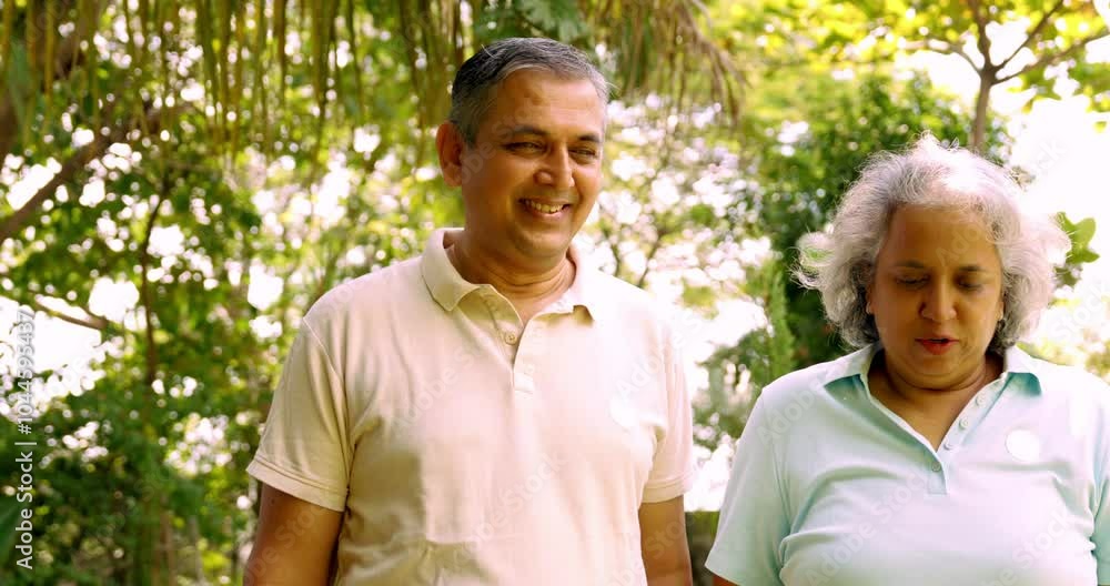 Indian Asian mid age couple in their fifties walking in the park, smiling and pointing, enjoying a pleasant conversation on a sunny day outdoors Indian Asian mid age couple in their fifties walking in the park, smiling and pointing, enjoying a pleasant conversation on a sunny day outdoors
