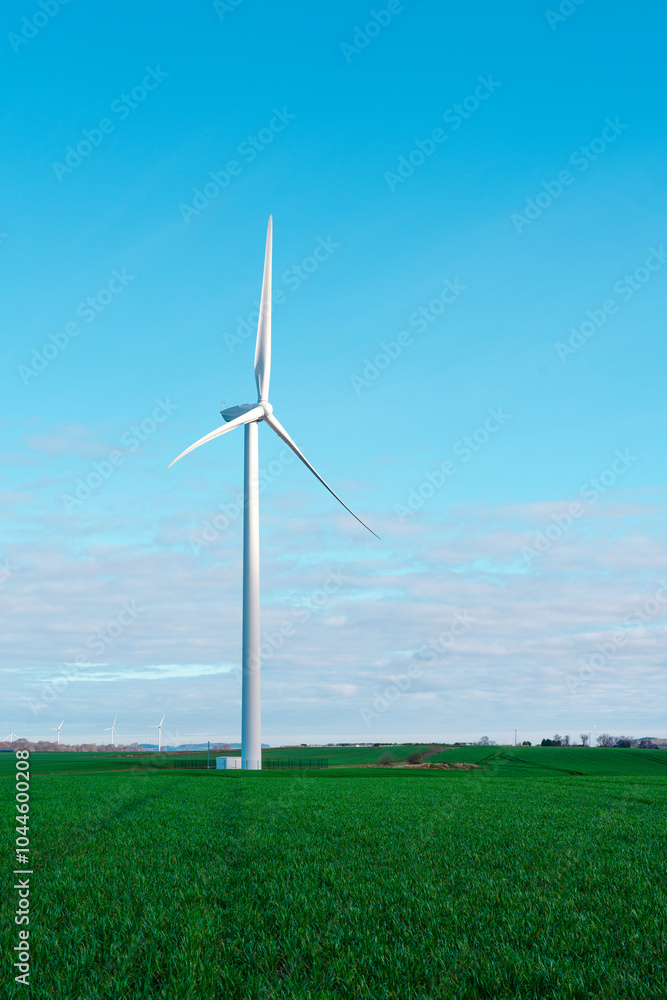 A single wind turbine stands tall against a bright blue sky in a lush green landscape on a calm day A single wind turbine stands tall against a bright blue sky in a lush green landscape on a calm day