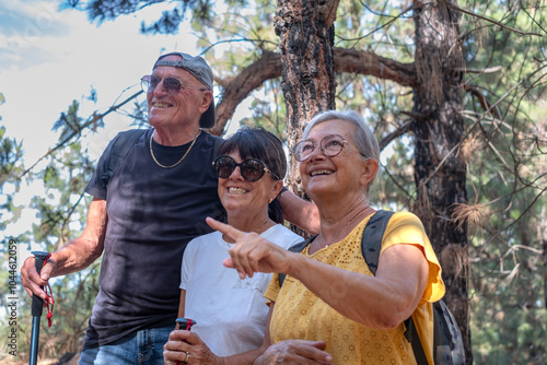 Happy group of senior friends enjoying vacation and adventure trekking in the forest, two elderly women and one man looking at landscape smiling. Sport, freedom, healthy lifestyle concept #1044612059