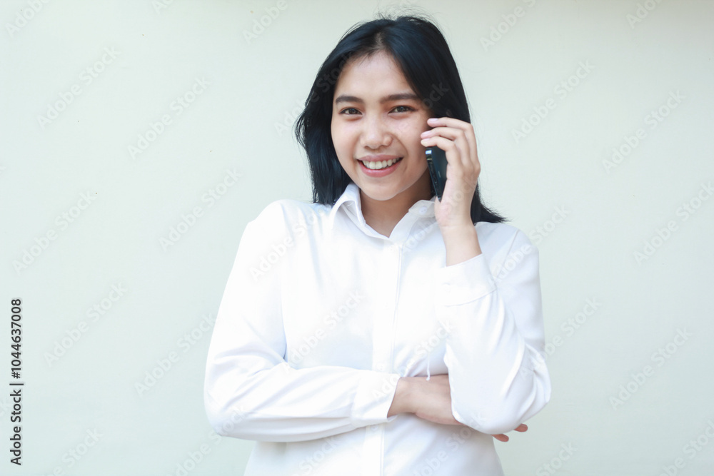 portrait of confident young asian business woman speaking on smartphone with arms folded looking at camera smiling peaceful wearing white formal suit shirt, standing isolated, wireless conversation portrait of confident young asian business woman speaking on smartphone with arms folded looking at camera smiling peaceful wearing white formal suit shirt, standing isolated, wireless conversation