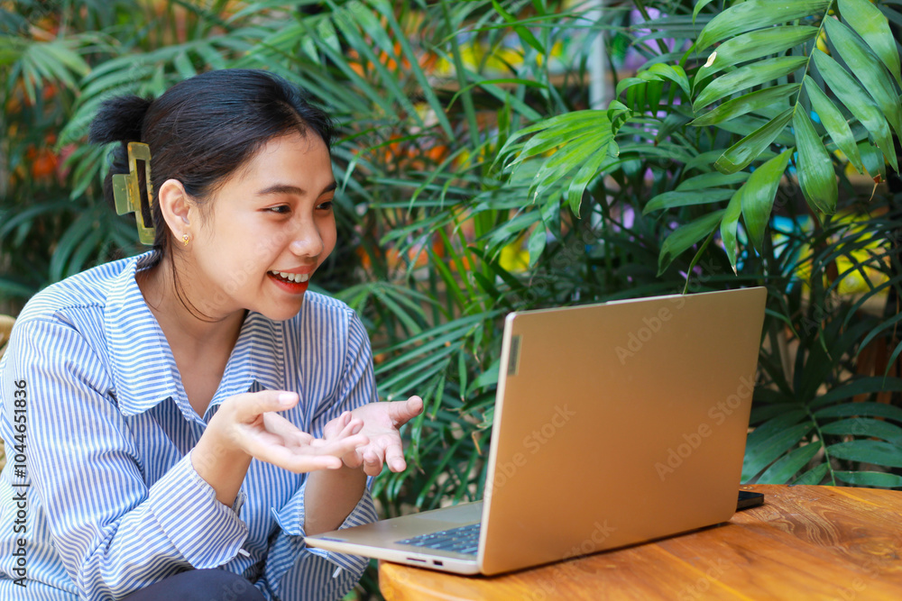 excited asian woman sitting in outdoor cafe with green plant interior using laptop working from anywhere, talking on computer have online meeting video chat excited asian woman sitting in outdoor cafe with green plant interior using laptop working from anywhere, talking on computer have online meeting video chat