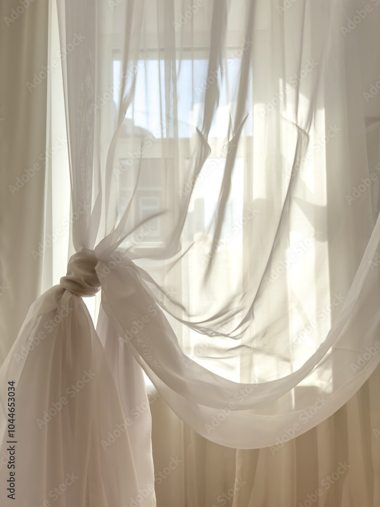 A white curtain with a knot tied to it is hanging in front of a window A white curtain with a knot tied to it is hanging in front of a window