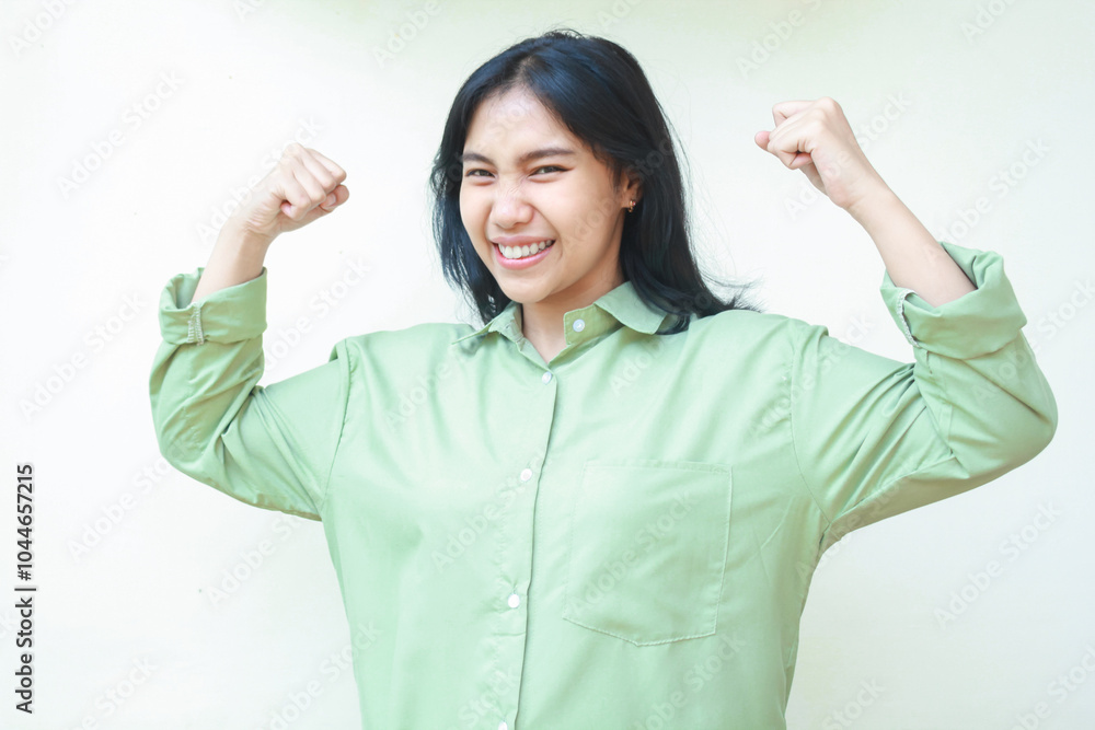 playful success dark hair asian woman laughing and dancing to celebrate champion win victory by raise fist wearing green oversize shirt standing over isolated white background, looking at camera playful success dark hair asian woman laughing and dancing to celebrate champion win victory by raise fist wearing green oversize shirt standing over isolated white background, looking at camera
