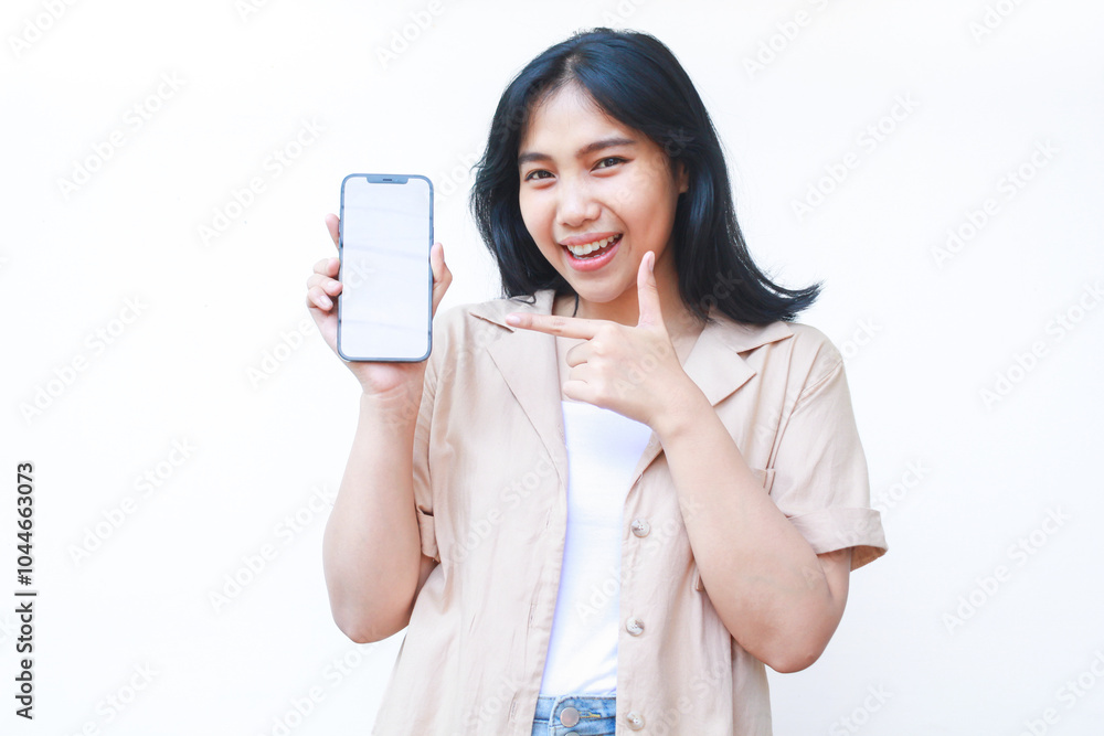 excited asian woman do presenting gesture with pointing finger to smartphone white screen wearing brown casual clothes isolated on white background excited asian woman do presenting gesture with pointing finger to smartphone white screen wearing brown casual clothes isolated on white background