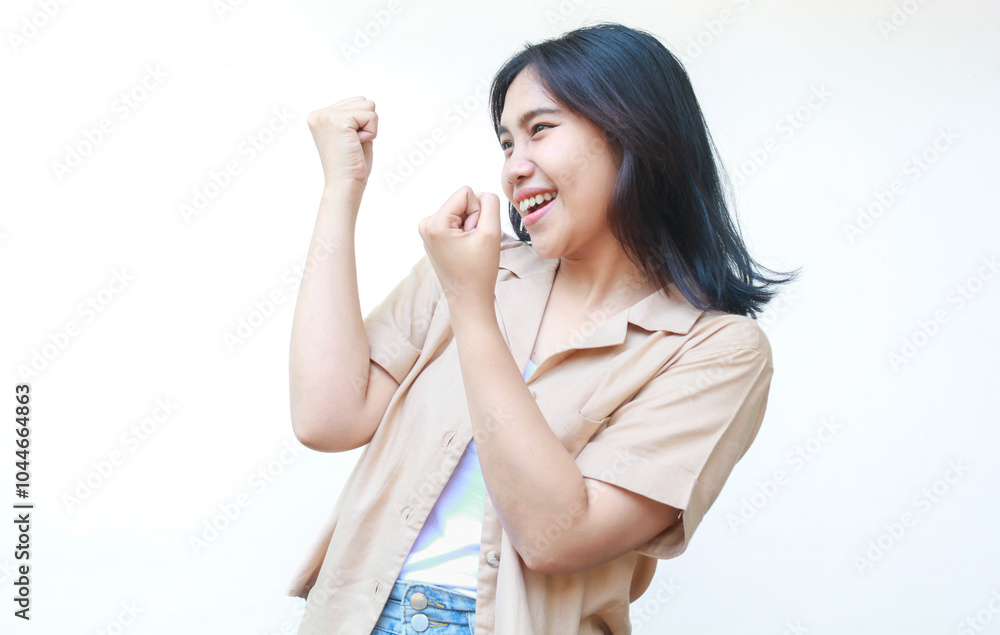 happy asian woman celebrate victory with raised fist wearing casual brown clothes isolated on white background happy asian woman celebrate victory with raised fist wearing casual brown clothes isolated on white background