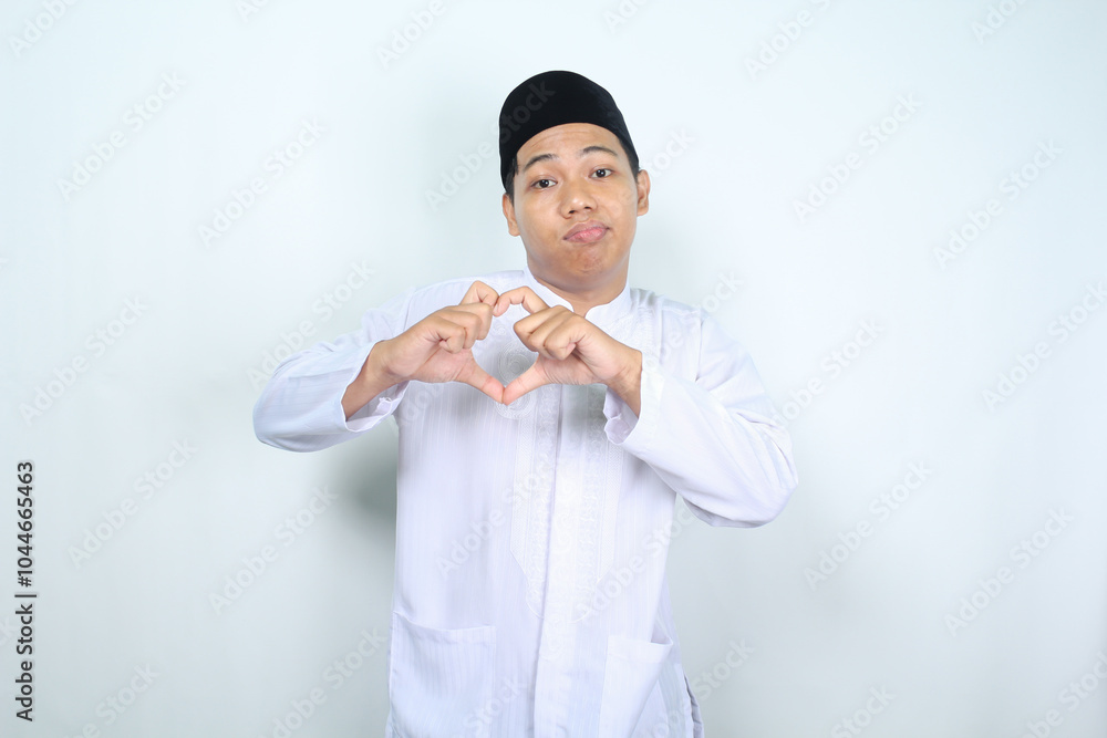 unhappy asian muslim man looking at camera and show heart shape isolated on white background unhappy asian muslim man looking at camera and show heart shape isolated on white background