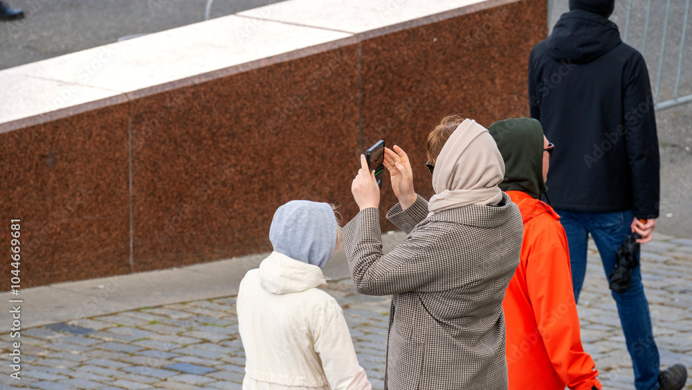 A woman in autumn clothes in a coat and scarf takes photographs of the sights in the city. A woman in autumn clothes in a coat and scarf takes photographs of the sights in the city.