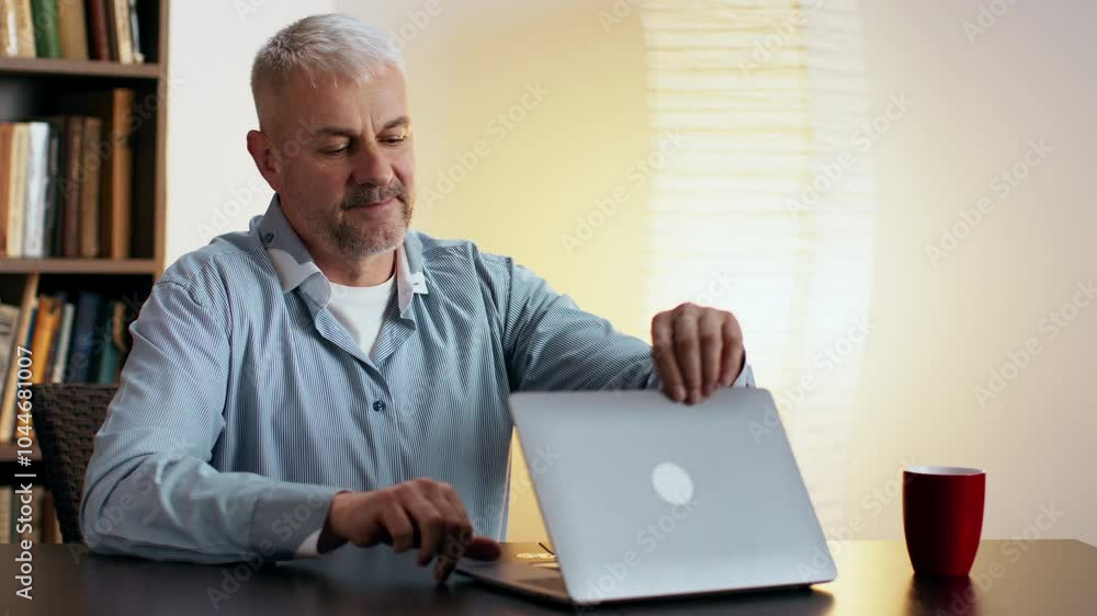 A man engages in a video call while seated at a table, dressed comfortably, with a warm, inviting background. A man engages in a video call while seated at a table, dressed comfortably, with a warm, inviting background.