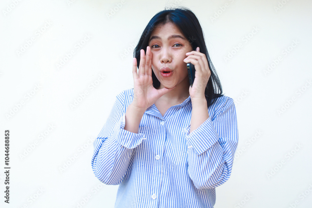 excited asian woman wearing striped shirt using smartphone screaming isolated on white background excited asian woman wearing striped shirt using smartphone screaming isolated on white background