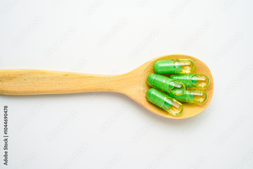 transparent capsules pills with a mixture of green powder and oil in wooden spoon, vitamin supplements transparent capsules pills with a mixture of green powder and oil in wooden spoon, vitamin supplements