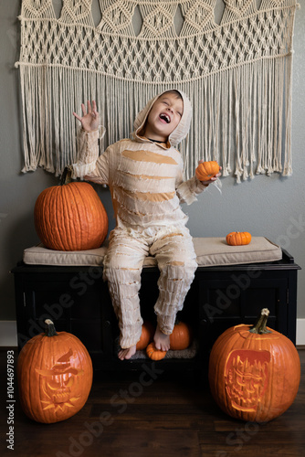 Child in mummy costume posing with pumpkins in Halloween scene indoors photo