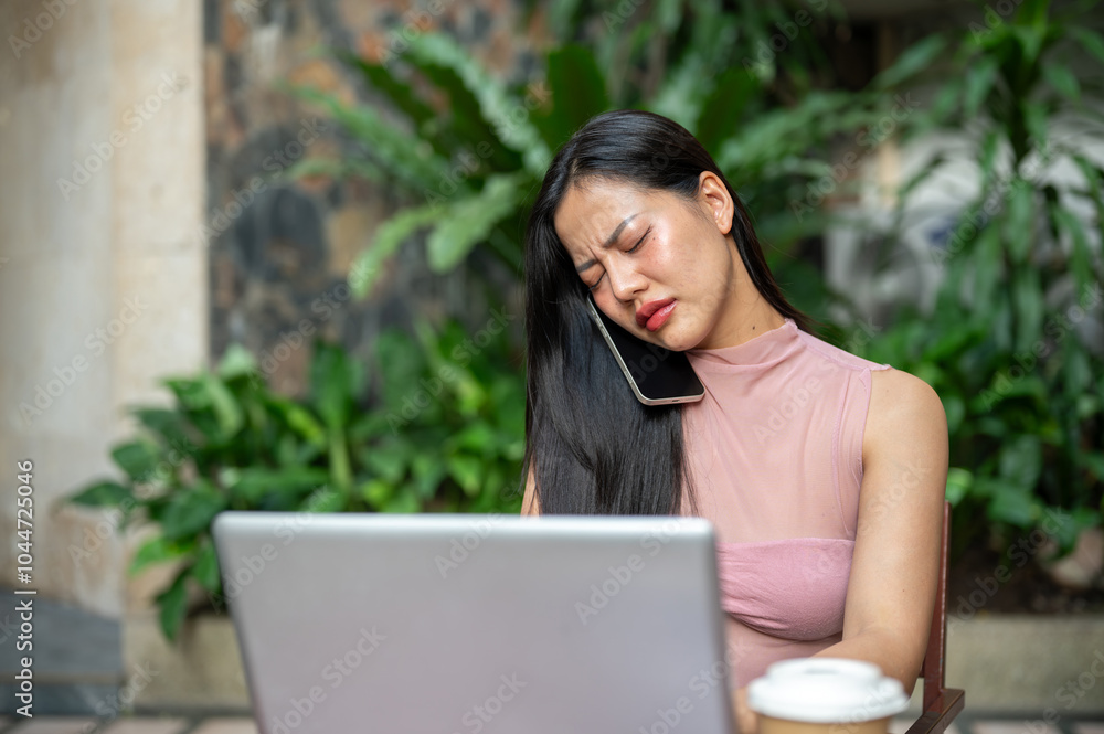 A stressed woman is having a serious phone conversation while working remotely from a coffee shop. A stressed woman is having a serious phone conversation while working remotely from a coffee shop.