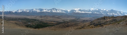 Panoramic high resolution image of Chuya steppe: hilly landscape, endless field with yellow grass, a golden autumn in the Altai. In the distance is a mountain ridge with snow covered mountain peaks. photo