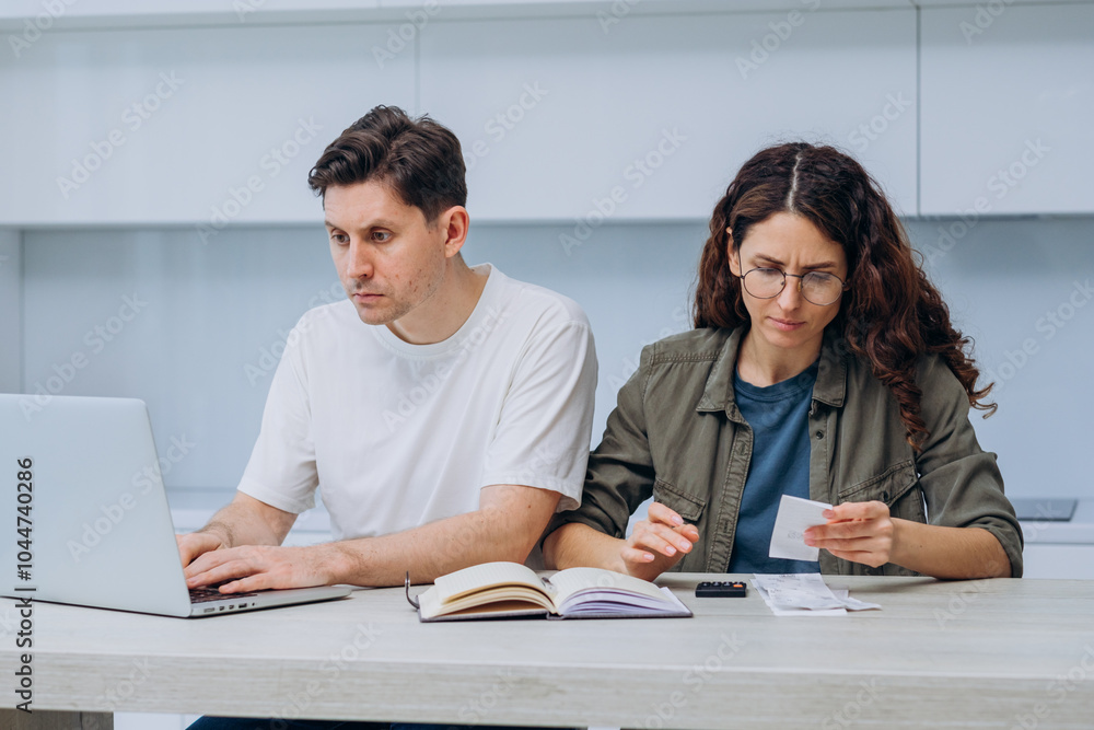 Young couple is sitting at their kitchen table, managing their finances together and looking concerned as they review bills and bank statements Young couple is sitting at their kitchen table, managing their finances together and looking concerned as they review bills and bank statements