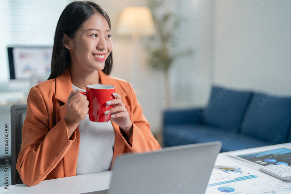 Young asian businesswoman is enjoying a coffee break at her home office, taking a moment to relax and reflect on her work Young asian businesswoman is enjoying a coffee break at her home office, taking a moment to relax and reflect on her work