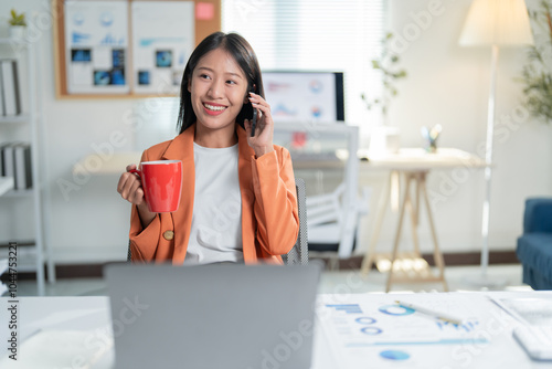 Young manager is working in her bright office, drinking coffee and talking on the phone while going over some documents