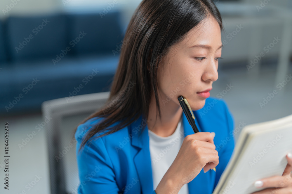 Focused young businesswoman in blue blazer, thinking and writing notes at organized office desk, planning business strategies for success Focused young businesswoman in blue blazer, thinking and writing notes at organized office desk, planning business strategies for success