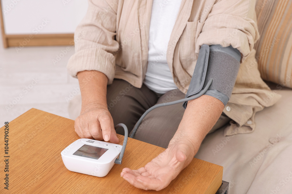 Fototapeta premium Senior woman measuring blood pressure at wooden table indoors, closeup