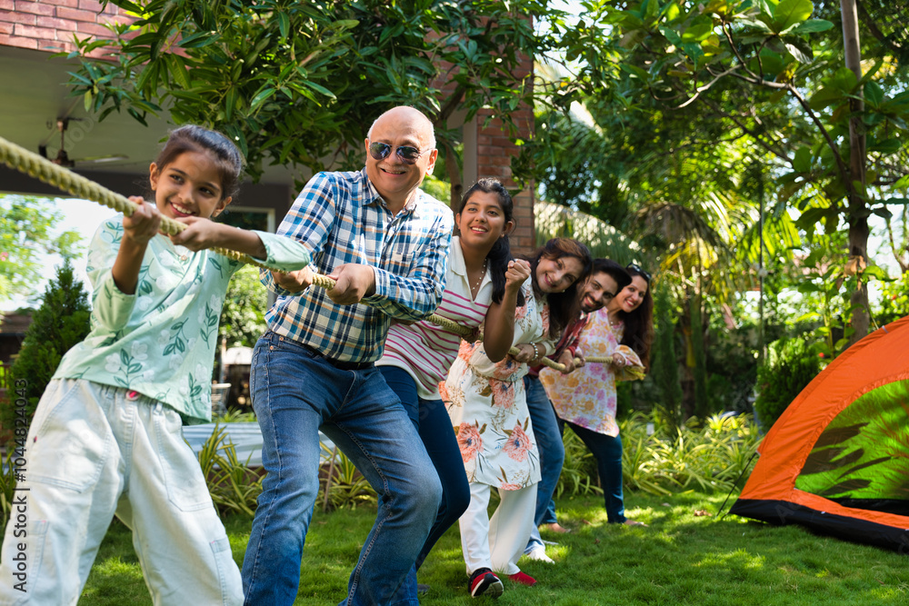 Fototapeta premium Indian family of six enjoying a fun outdoor camping game of tug of war, bonding, creating memories