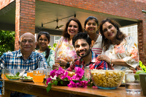 Canvas Print Indian family enjoying breakfast outdoors, happily posing for a group photo arou