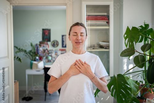 Relaxed woman feeling heartbeat, hands on chest, meditating deeply at home. Focused breathing, mindfulness practice, self reflection, calming atmosphere, serenity in solitude and health, body care