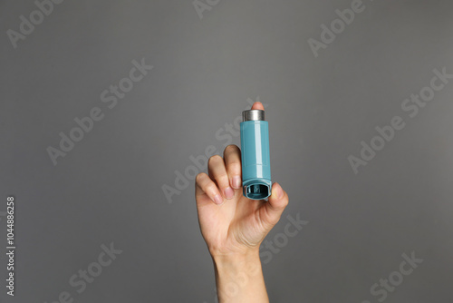 Woman holding asthma inhaler on grey background, closeup photo