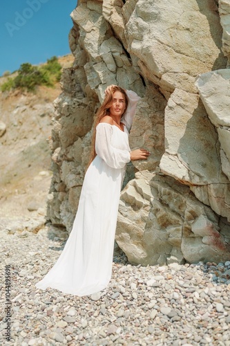 A woman in a white dress is standing on a rocky beach. Concept of serenity and tranquility, as the woman is enjoying the natural beauty of the beach.