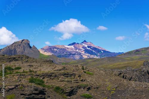 Scenic view on snow covered peak of Ymir with Rhino shape rock on left and scenic volcanic icelandic nature during beautiful day and blue sky with clouds when hiking Laugavegur trail near Thorsmork